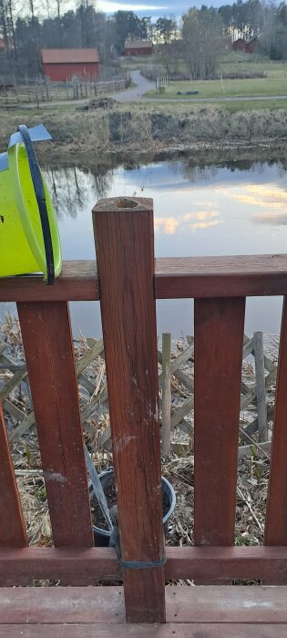 Delvis uthölt trästolpe på en altan med tecken på röta vid en sjö, säkerhetshjälm i förgrunden.