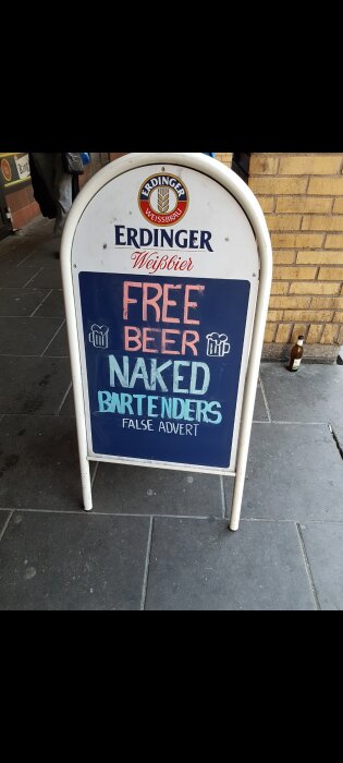 Gatuskylt med texten "FREE BEER, NAKED BARTENDERS, FALSE ADVERT" och en ölflaska på trottoaren.