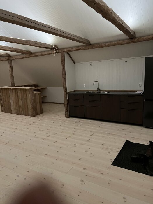 Renoverat lantligt rum med synliga takbjälkar, trädgolv, pentry och hembyggd bar av återanvänt material.
