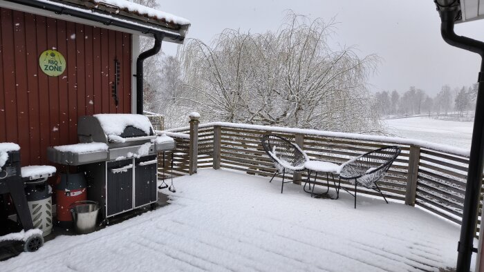En snötäckt uteplats med grill och möbler, träd och öppet landskap i bakgrunden.