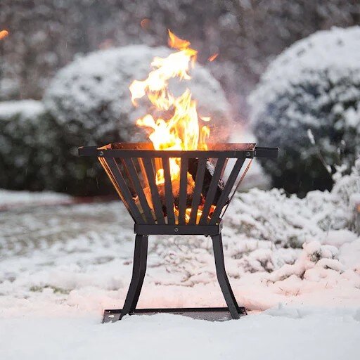 Eldkorg med brinnande eld på en snöig trädgård.