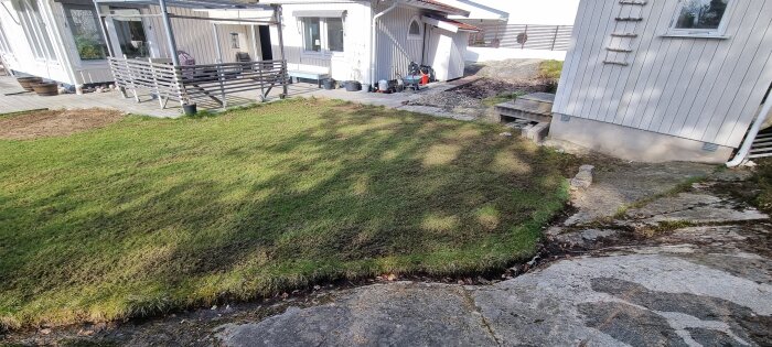 Gräsmatta med stående vatten framför hus, gulmarkerade områden, på bergig grund.