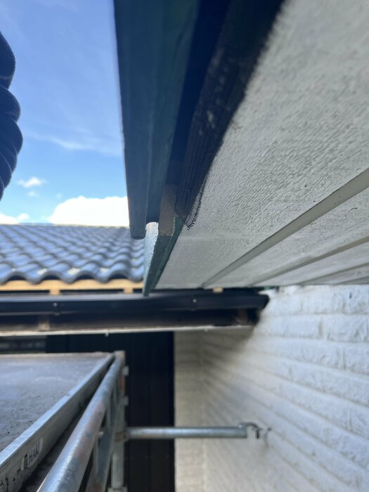 Undersida av tak med skivor som är överlappade oregelbundet under hängrännan vid husvägg.