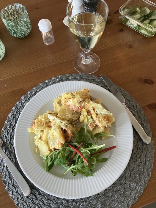 Tallrik med laxpudding och sallad, ett glas vitt vin och salladsskål på träbord.