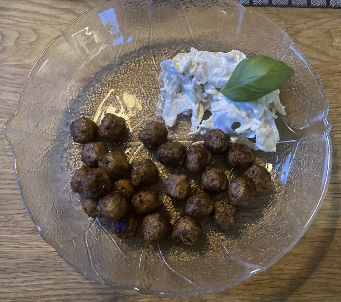 Stekt köttbullar och potatissallad på genomskinlig tallrik, serverad med basilikablad.