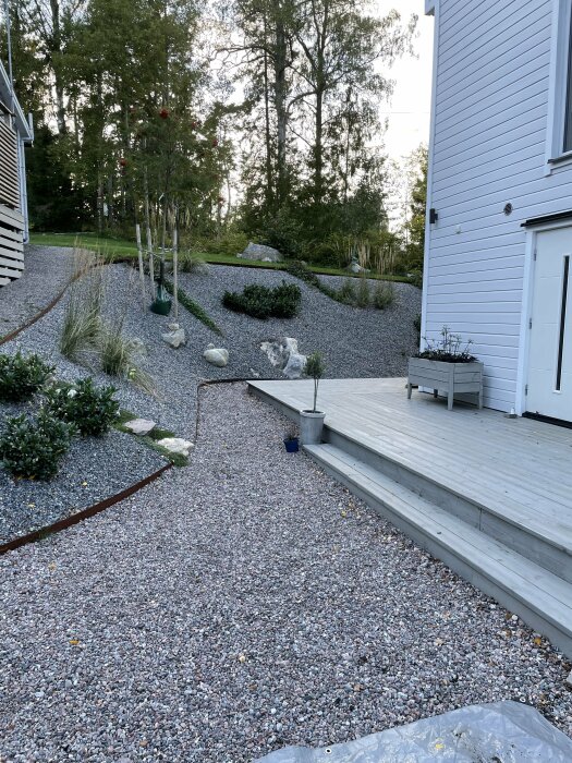 Renoverad trädgårdsslänt med cortenstål, grusväg och stenar intill vit husfasad.