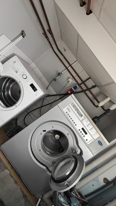 Tvättstuga under renovering med tvättmaskin och torktumlare, ommålade rör och kablar syns.
