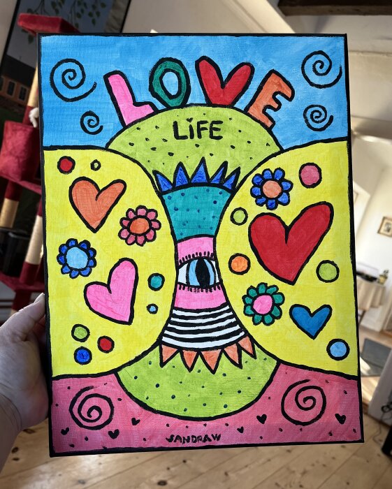 Färgstark målning med ordet "LOVE", hjärtan, blommor och mönster, hållen av en person.