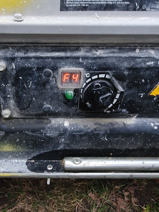 Display på en värmare som visar 4 grader Celsius, smutsig och fläckig med indikation på tekniskt fel.