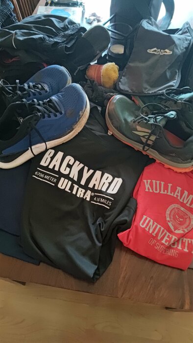 Löparkläder och skor med texten "BACKYARD ULTRA" och "KULLAMÄN UNIVERSITY OF SUFERING" på t-shirtar.