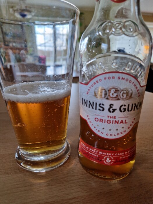 Delvis tömd flaska av Innis & Gunn öl bredvid ett glas med öl på en bordsskiva.
