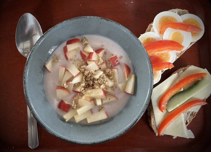 Skål med yoghurt och äppelbitar, smörgås toppad med ost, tomat och gurka.