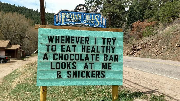 Humorskylt utanför Indian Hills Community Center med texten: "Whenever I try to eat healthy a chocolate bar looks at me & snickers".