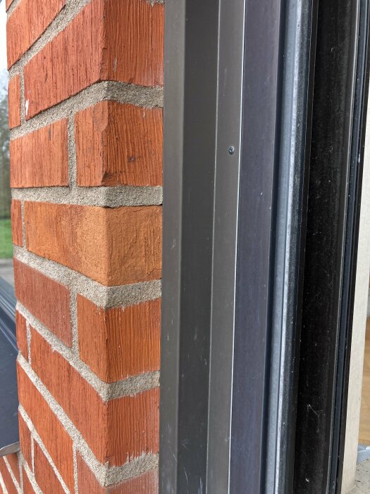 Fönster utan lister monterat dikt mot en tegelvägg med synlig aluminiumlist på utsidan.