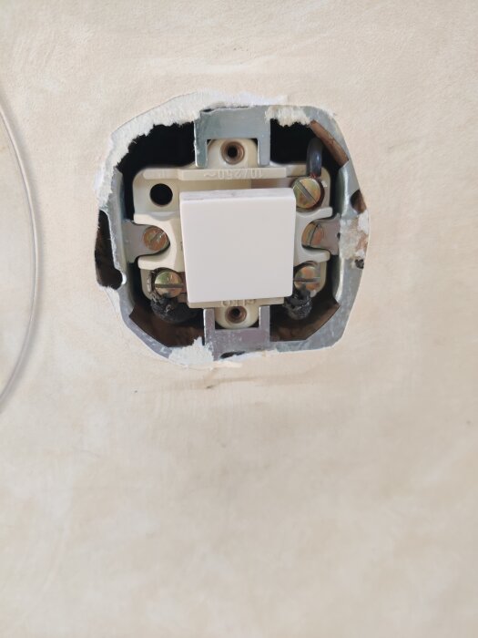 En öppen väggströmbrytare utan kåpa med en synlig enpolig mekanism och ledningar, infäst i väggen.