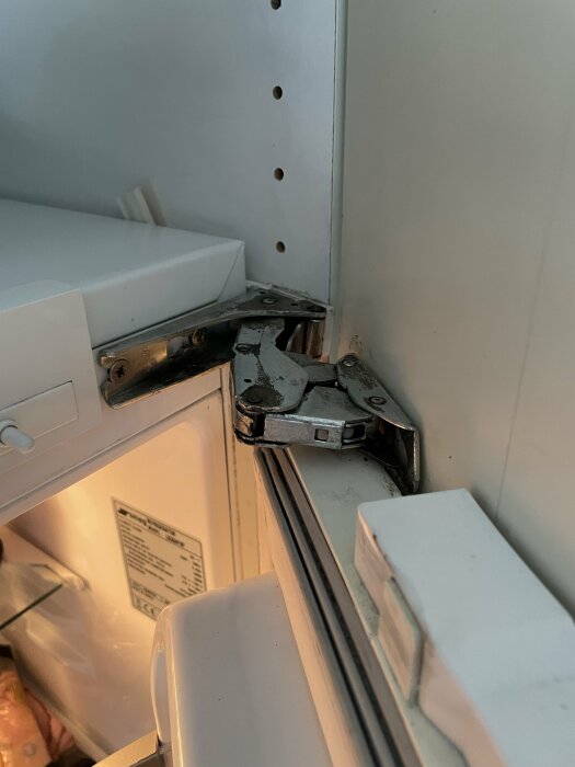 Slitet gångjärn på en Smeg kylskåpsdörr i ett kök, behöver ersättas på grund av tröghet och missljud.