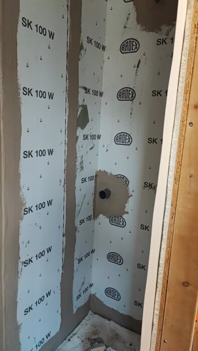 Vägg med tätskikt märkt "ARDEX SK 100 W", utskärning för avlopp, i pågående renoveringsprojekt.