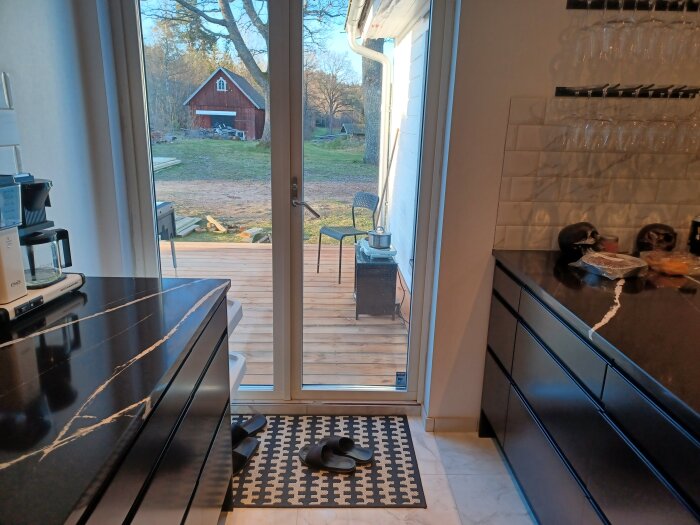 Kök med öppen dörr mot altan där en grill står redo, potatisbakelser syns innanför.