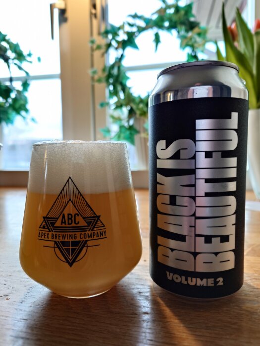Ett glas öl bredvid en burk med texten "BLACK IS BEAUTIFUL", inomhus mot ett fönster.