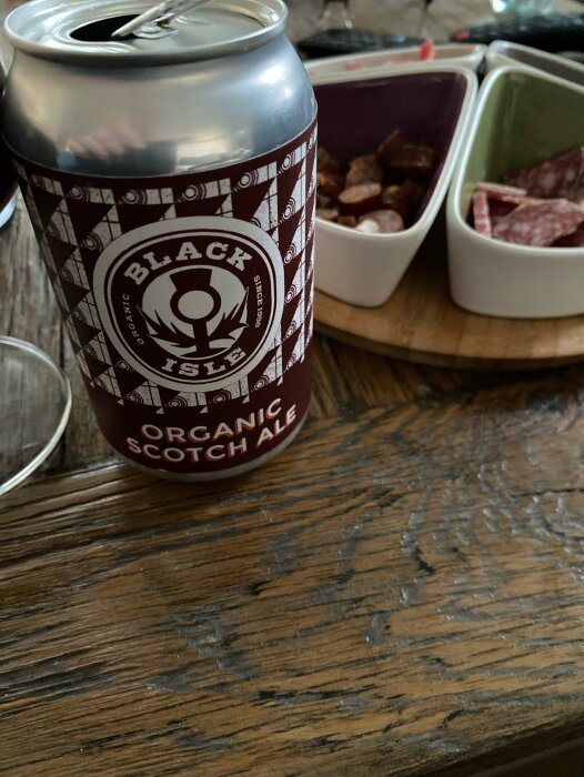 Burk med skotsk ale och små skålar med snacks på ett träbord.