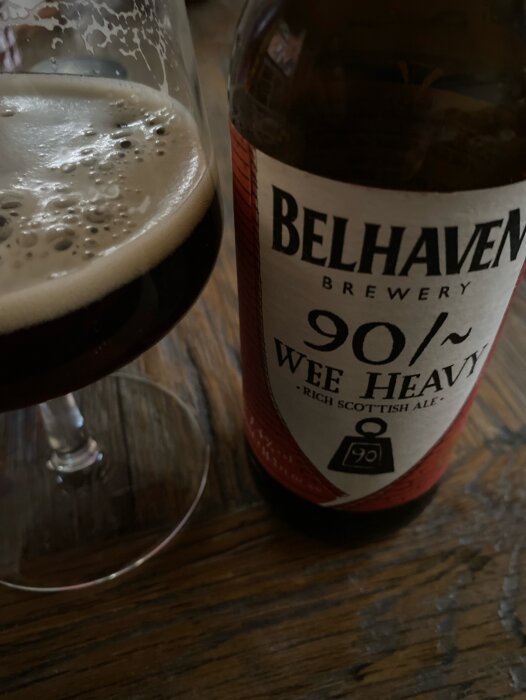 En närbild på ett glas och en Belhaven Wee Heavy-flaska på ett träbord.