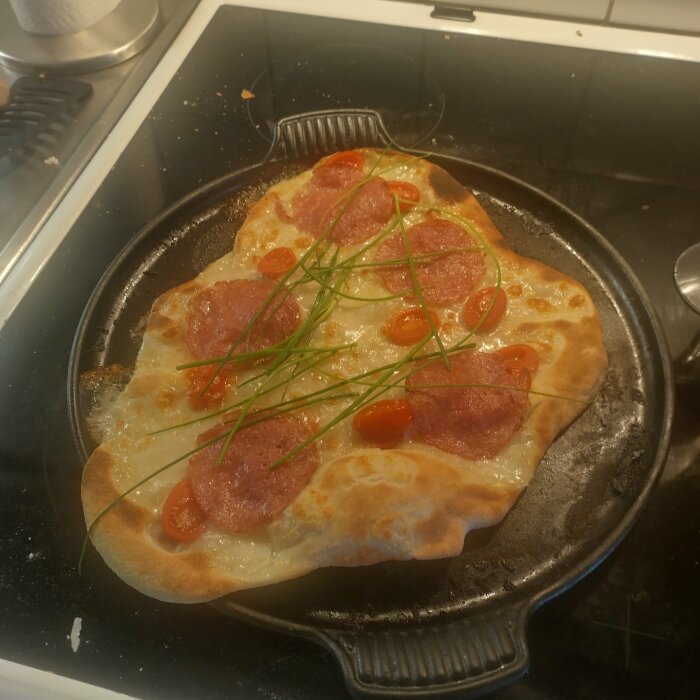 Hemlagad pizza med salami, körsbärstomater och gräslök på en ugnsplåt.