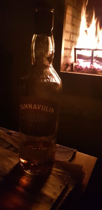 Flaska med single malt scotch whisky framför en öppen spis med flammor.