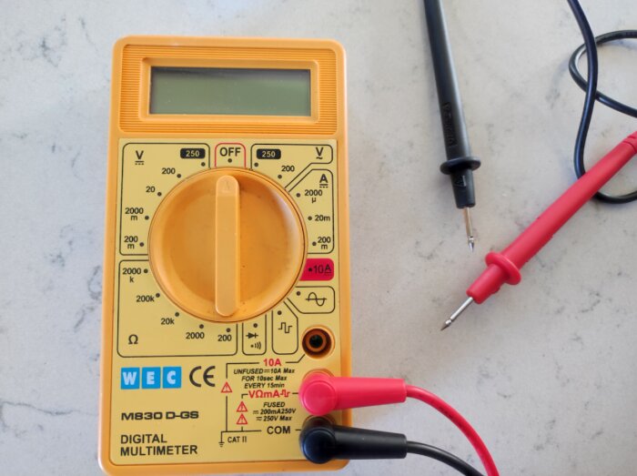 Digital multimeter på marmorlik yta med röd och svart mätprobe.