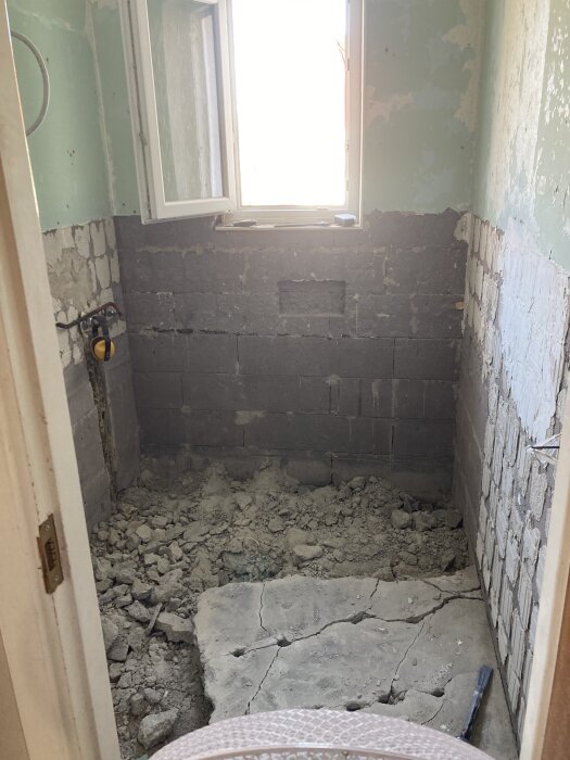 Delvis rivet badrum med blåbetongväggar och krossat golv synligt från dörröppning.
