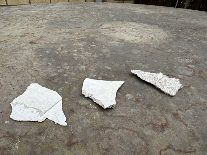 Fragment av vit puts från en äldre fasad ligger på en stenbelagd yta, behov av reparation synligt.
