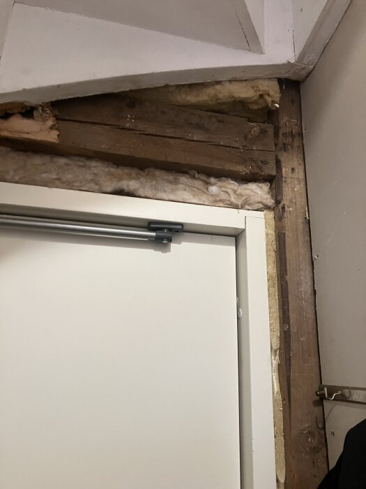 En ofärdig källardörr med synliga isoleringsmaterial och träbjälkar.