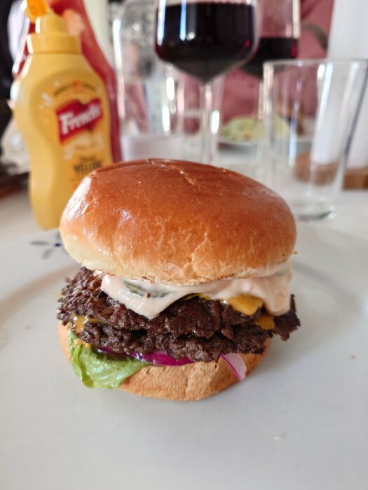 Smashburgare med dressing, cheddarost och picklad lök på tallrik, ketchup och senap i bakgrunden.