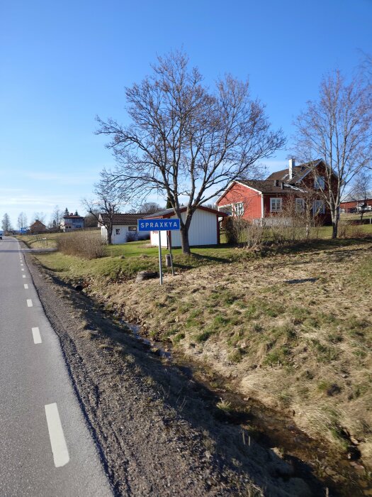 Landväg med skylt som säger "SPRÅKKYA", nakna träd och ett rött hus i bakgrunden.