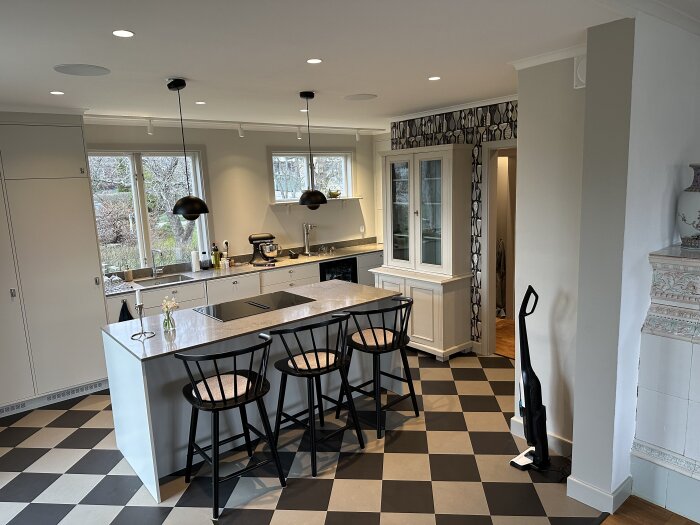 Renoverat kök med svartvit schackrutigt golv, köksö med barstolar och hängande lampor.