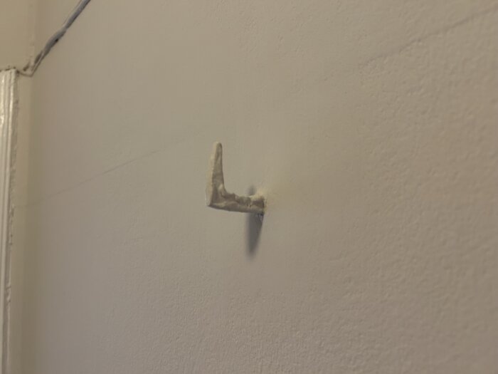 Övermålad gammal krok som sticker ut från en vägg i en hall.