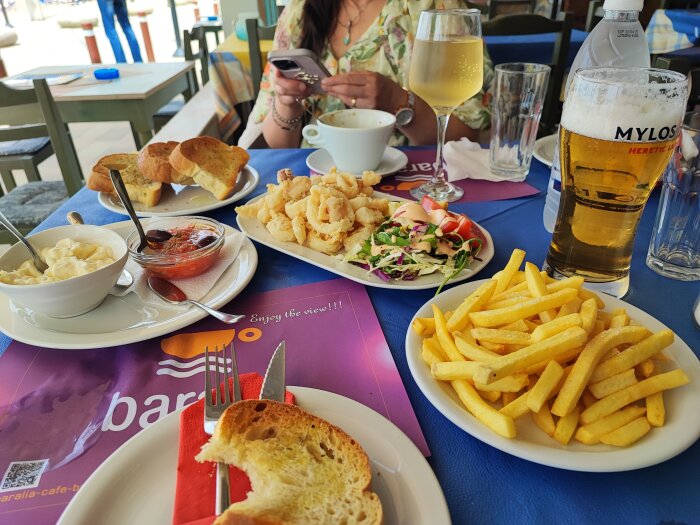 Måltid med calamares, pommes frites, aioli, en sallad, bröd, öl och ett glas vin på ett bord.