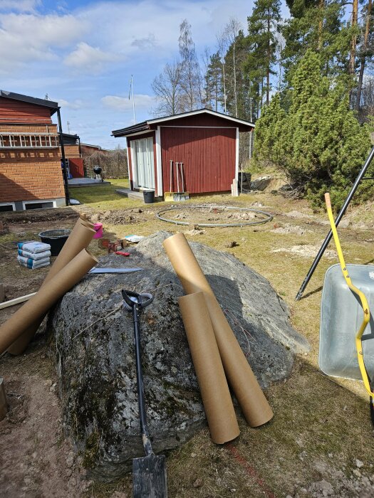 Altanbygge med stor sten täckt av mossa och byggmaterial runtomkring på en hustomt.