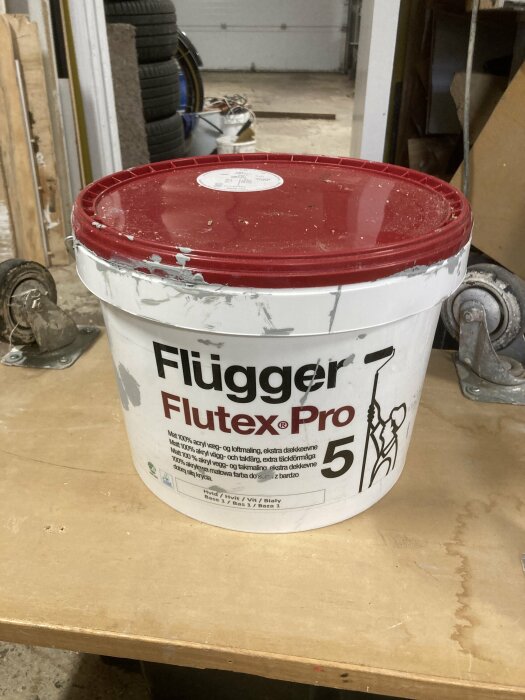 En hink med Flügger Flutex Pro färg på ett stökigt arbetsbord.