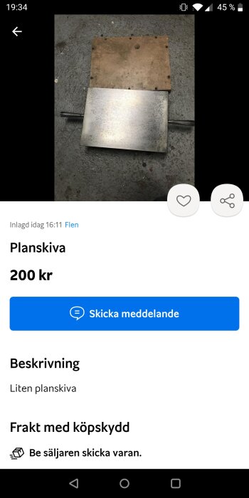 Begagnad liten planskiva av metall med trähandtag på grått underlag.