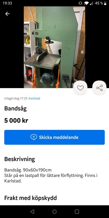 Grön bandsåg på en lastpall i ett garage, omgiven av verktyg och utrustning.