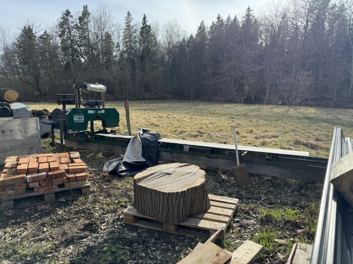 Trästock och plankor utomhus bredvid en bärbar sågkvarn, redo för att tillverka en soffa.