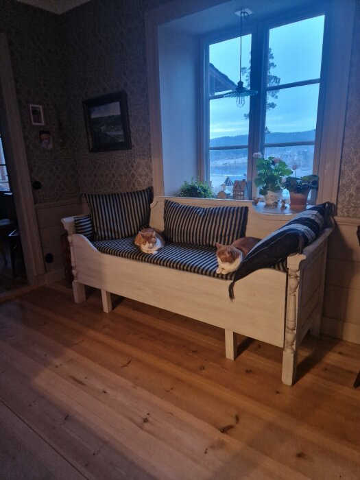 Vit träsoffa med randiga kuddar och två katter som ligger på, i ett inrett vardagsrum.