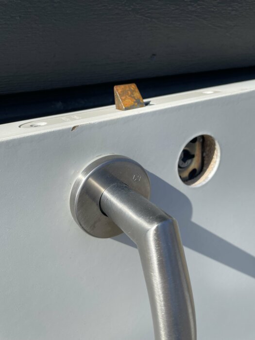 Handtag monterat på dörr med dolda skruvar och låsmekanism synlig genom hål i dörren.