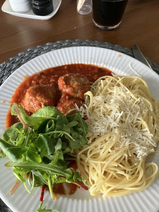 Tallrik med italienska köttbullar i tomatsås, spaghetti, riven parmesan och sallad.