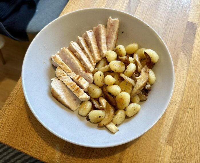 Tallrik med gnocchi, stekt ostronskivling och skivad tonfisk på ett träbord.