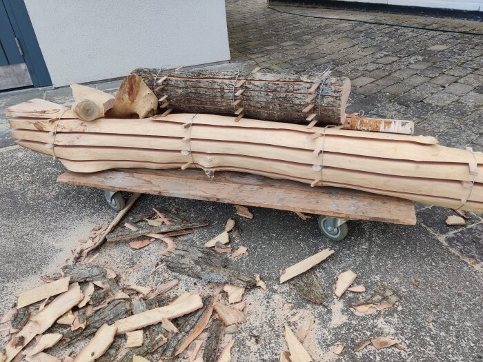 Hyvelade träplankor och råa trädgrenar på en vagn omgiven av spån och bark.