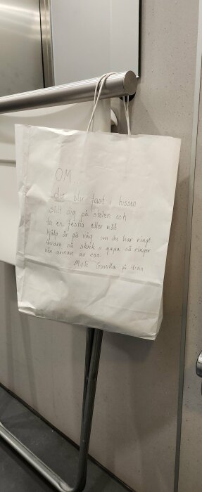 Papperskasse hängande på en rund metallstång med handskriven text som ger instruktioner för vad man ska göra om man blir fast i hissen.