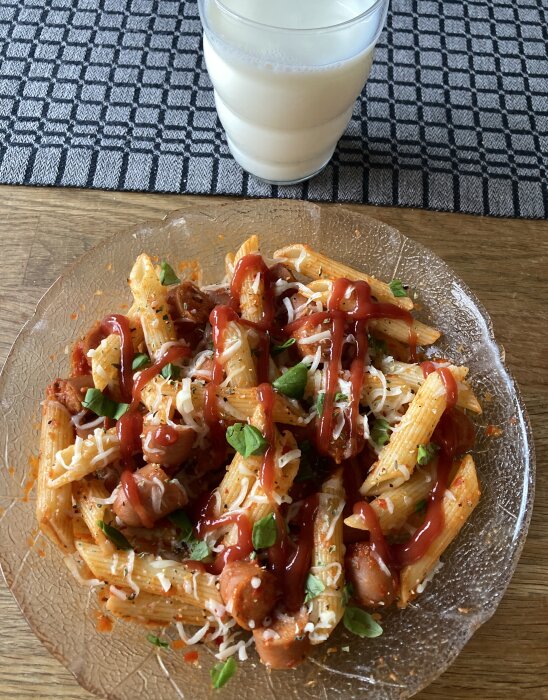 Penne-pasta med ajvar, mozzarella, kryddor och korvbitar på tallrik, serverad med ett glas mjölk.