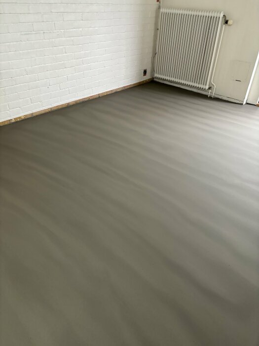 Ojämnt flytspacklat golv med zebraliknande skiftningar mot vit tegelvägg och en radiator.