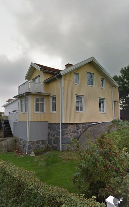 Gult charmigt hus från 1906 med sadeltak och krypgrund på en sluttande bergstomt.